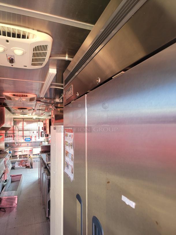 Interior of a commercial food truck featuring stainless steel appliances, prep area, overhead air vents, and visible operational guidelines.
