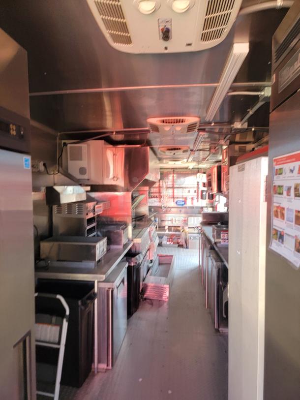 Commercial kitchen interior with stainless steel appliances, refrigeration units, and overhead ventilation. Clean and well-maintained.