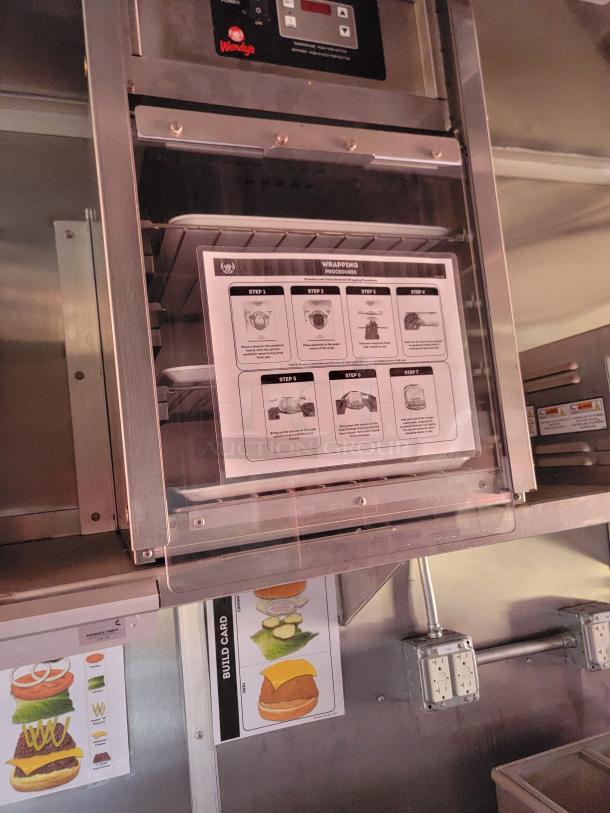 Commercial warming drawer system with control panel, featuring Wendy's branding. Includes instructions for food wrapping procedures.
