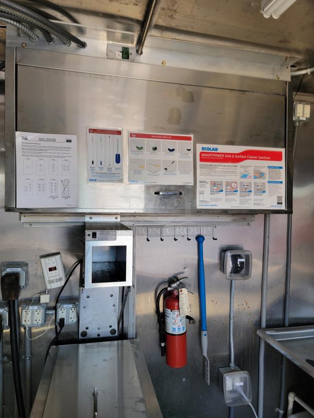 Commercial kitchen wall with Ecolab cleaning instructions, electrical switches, fire extinguisher, and utensils for sanitation.