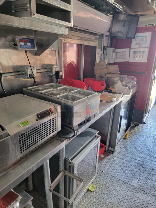 Food truck interior featuring stainless steel kitchen equipment, including a refrigeration unit, food warmer, and prep area.