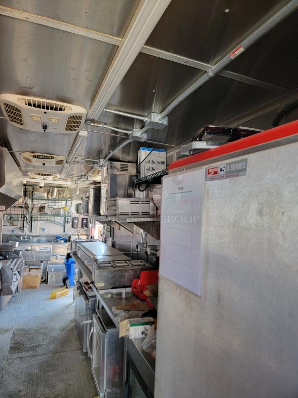 Interior of a commercial kitchen trailer with stainless steel countertops, refrigeration units, and ventilation systems. Clean and organized.