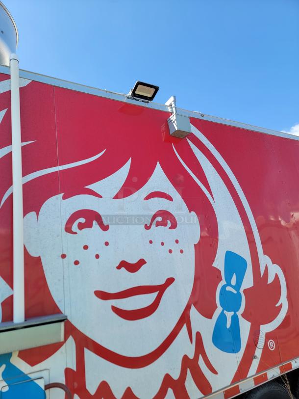 Close-up of a Wendy's truck with the iconic red-haired logo against a bright blue sky. The truck appears in good condition.