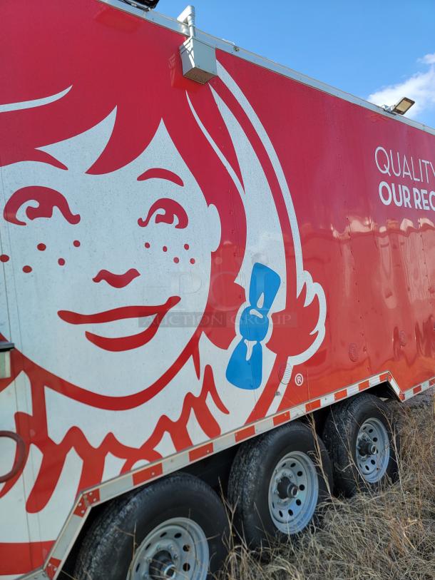 Red and white trailer with Wendy's logo, featuring girl with red hair. Visible text: "QUALITY OUR REC." Triple-axle wheels in grassy area.