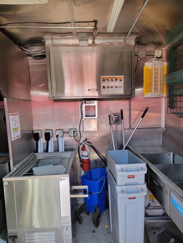 Stainless steel kitchen setup with storage units, ice machine, fire extinguisher, and waste bins; suitable for food service.