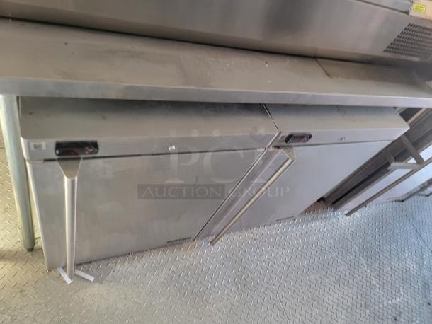 Stainless steel commercial refrigerator with double swing doors. Features top cooling vents. Surface shows wear.