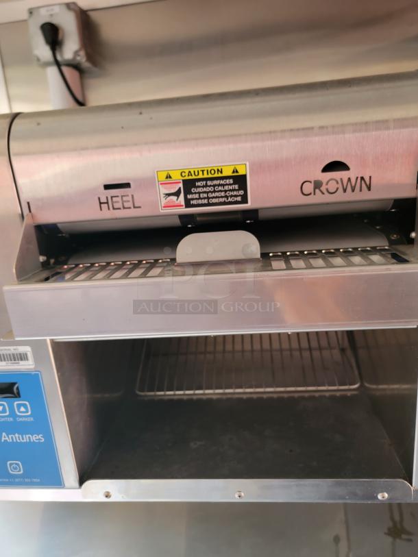 Antunes commercial toaster with "HEEL" and "CROWN" labels, caution sign indicating hot surfaces. Features adjustable darkness settings.
