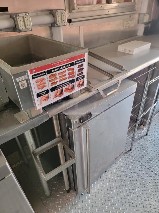 Commercial kitchen setup with a stainless steel deep fryer and a small fridge. Fryer has bacon cooking guide on it.