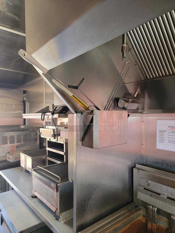 Commercial kitchen griddle setup with dual-fryer, stainless steel surfaces, ventilation hood, and utensil holder, in good condition.