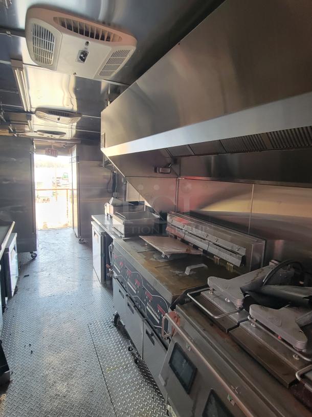 Commercial kitchen interior with stainless steel appliances, including grills and fryers. Visible wear on surfaces.