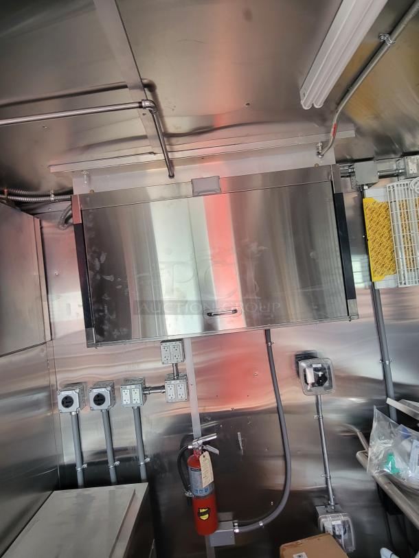 Commercial kitchen interior with stainless steel surfaces, electrical outlets, a fire extinguisher, and wiring.