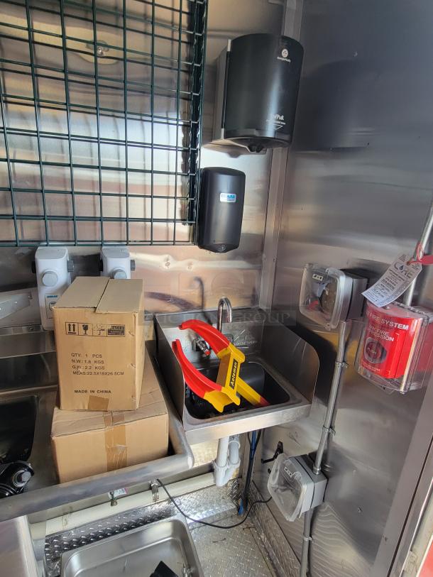 Commercial stainless steel kitchen setup with sink, Ecolab soap dispenser, cardboard boxes, and fire system control panel.