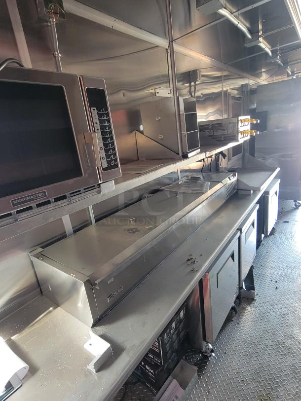 Stainless steel commercial kitchen setup with multiple appliances, including microwaves and prep tables, in used condition.