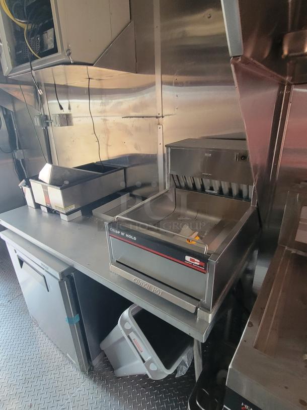 Commercial kitchen setup with Crisp N' Hold food warmer. Features include stainless steel design and "Caution Hot" label. Clean condition.