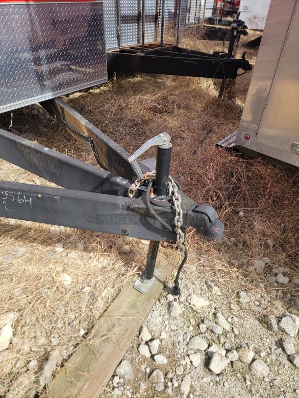 Trailer hitch with chains and jack stand on gravel. Metal is weathered. Chain and wiring visible.