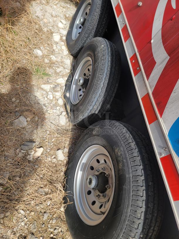 Dual axle trailer wheels with metal rims and visible treads, attached to a red and white trailer. Appears in good condition.