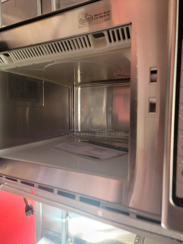 Stainless steel microwave interior with visible label indicating service contact information. Clean condition.
