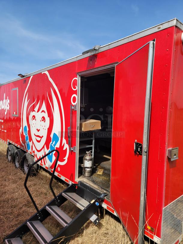 Red mobile kitchen trailer with Wendy's branding, open side door, three axles, and metal stairs. In used condition.