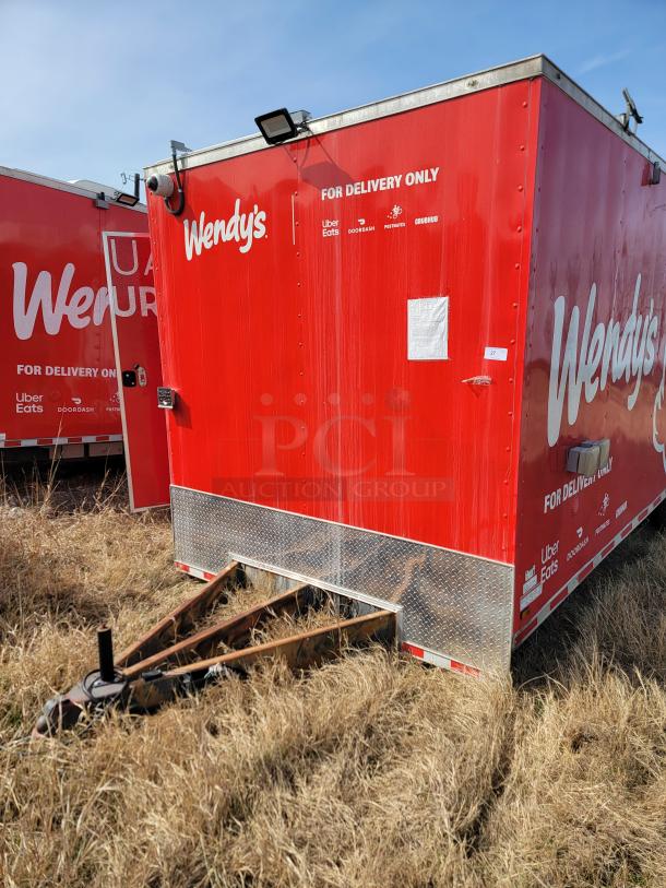 Red Wendy's delivery trailer with logos for Uber Eats, DoorDash, and Grubhub. Visible hitch, possibly unused in grassy field.