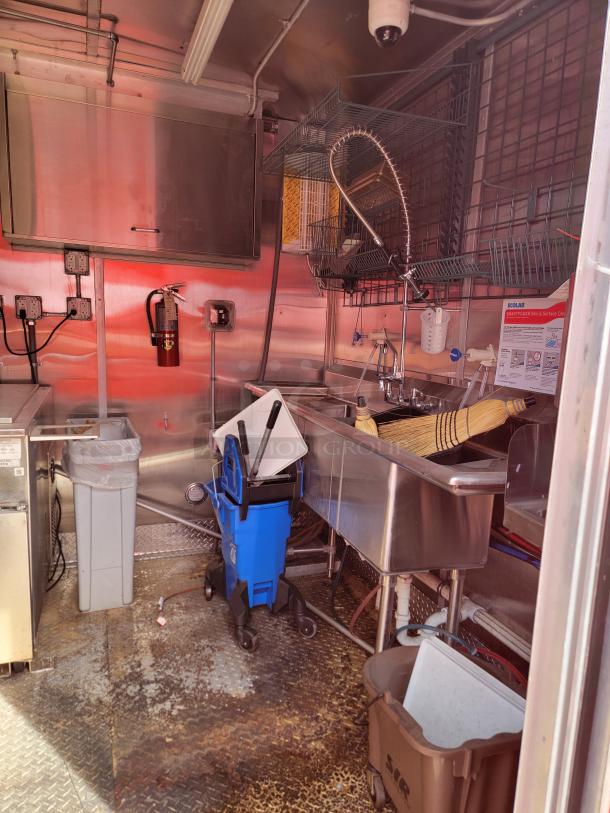 Commercial kitchen with stainless steel sink, storage shelves, mop bucket, and cleaning supplies. Interior of a food truck.