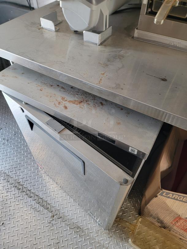 Commercial stainless steel warming drawer with visible surface rust and wear. QR code tag on top for scanning.
