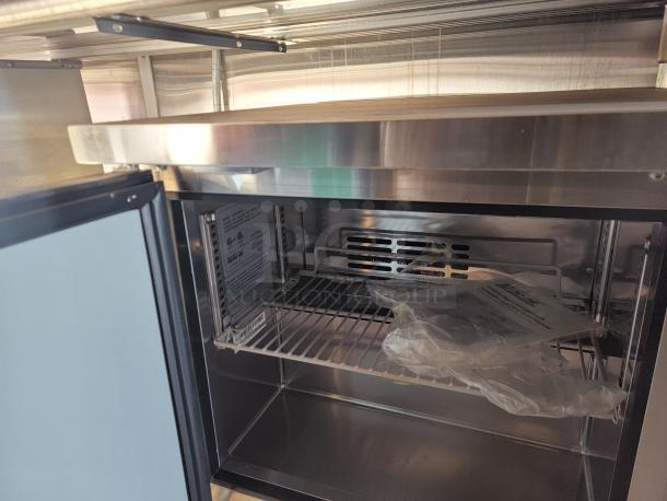 Commercial stainless steel refrigerator interior, featuring adjustable shelving, new condition, visible manual, and protective plastic.
