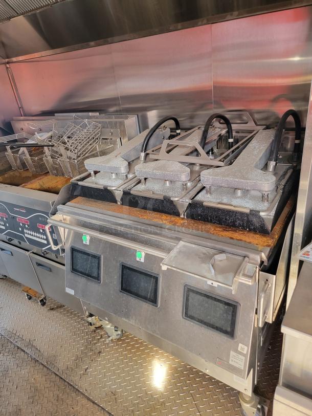 Commercial kitchen fryer setup with multiple fry baskets, digital displays, and control panels. Visible wear and stainless steel construction.