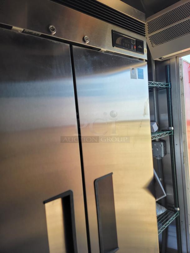 Stainless steel commercial refrigerator, dual doors with handles, digital temperature display, and manufacturer badges visible.