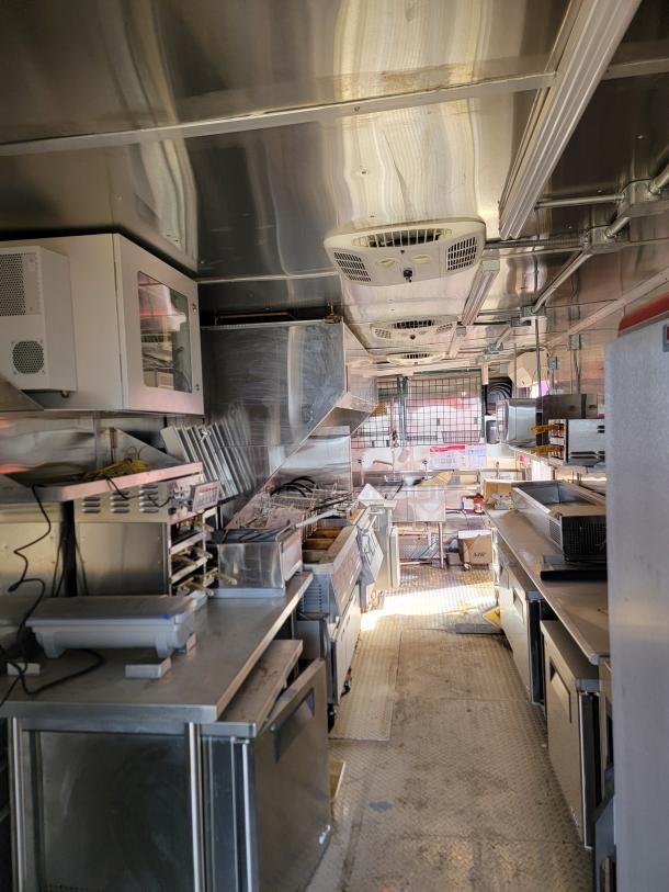 Interior of a commercial kitchen in a food truck, featuring stainless steel countertops, ventilation hoods, and cooking appliances. Clean and well-maintained.