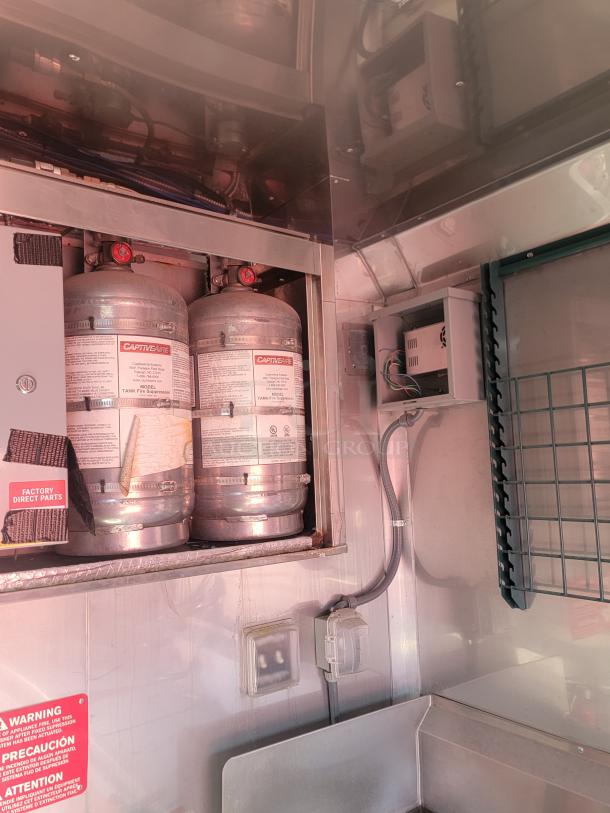 Two CaptiveAire fire suppression tanks inside a metal cabinet, labels visible indicating model and instructions.