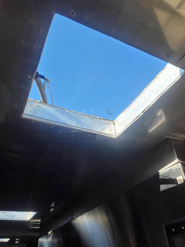 Large metal structure with open roof, showing sleek interior panels and a clear, blue sky above. No visible VIN.