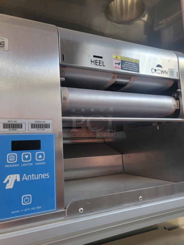 Antunes commercial toaster with "Heel" and "Crown" labels, blue control panel, and caution warning. Visible serial numbers.