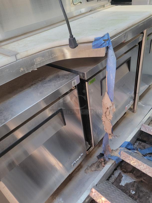 Stainless steel Avanti food prep table with refrigeration, visible wear, includes electrical outlet, taped section on surface.