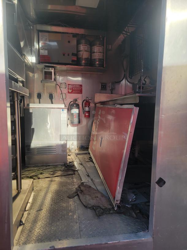 Interior of a mobile kitchen with stainless steel surfaces, fire extinguishers, and equipment. Visible signs of wear.