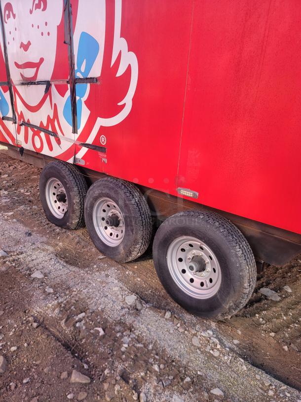 Red utility trailer with tri-axle wheels and branded logo. Condition shows signs of outdoor use; no visible VIN.