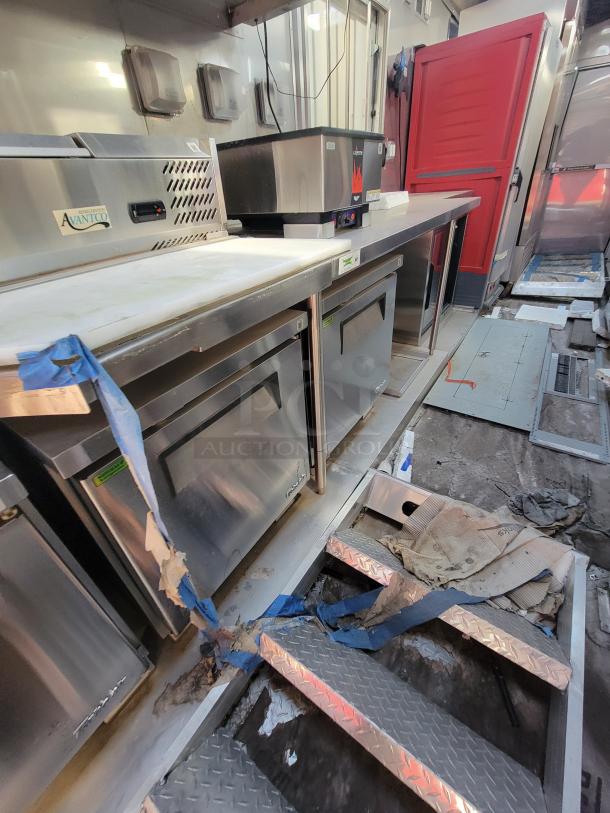 Commercial kitchen with Avantco equipment featuring refrigerators and countertops. Visible wear and construction debris.