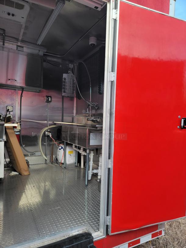 Mobile kitchen interior with stainless steel sink, red exterior door, diamond plate flooring, and plumbing fixtures visible.