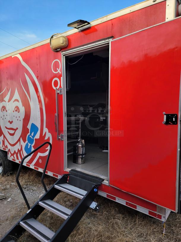 Red food truck with recognizable logo, side stairs, and partially open door revealing interior kitchen equipment.