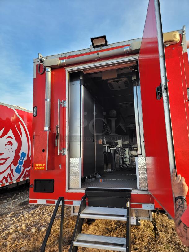 Red food truck with open rear door, metal steps, and visible kitchen interior. Features security camera and electrical markings.