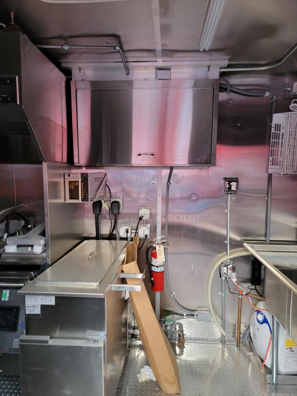 Commercial kitchen equipment with stainless steel surfaces, outlets, and a mounted fire extinguisher. Ideal for mobile kitchens.
