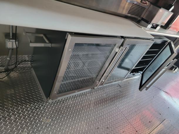 Stainless steel under-counter glass door refrigeration unit with two sections, visible shelving, and open door, in good condition.