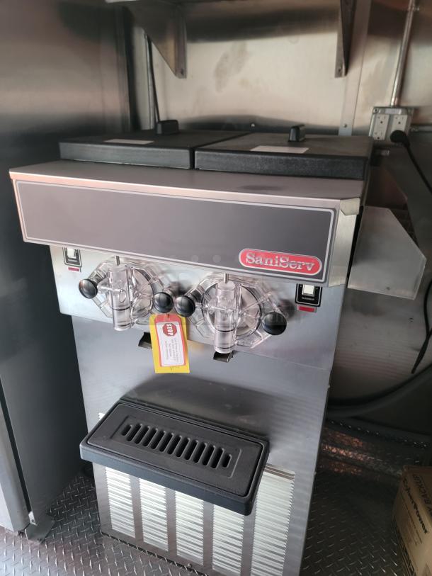 SaniServ soft serve machine, stainless steel, dual handles, excellent condition, visible "Stop" tag for maintenance checks.