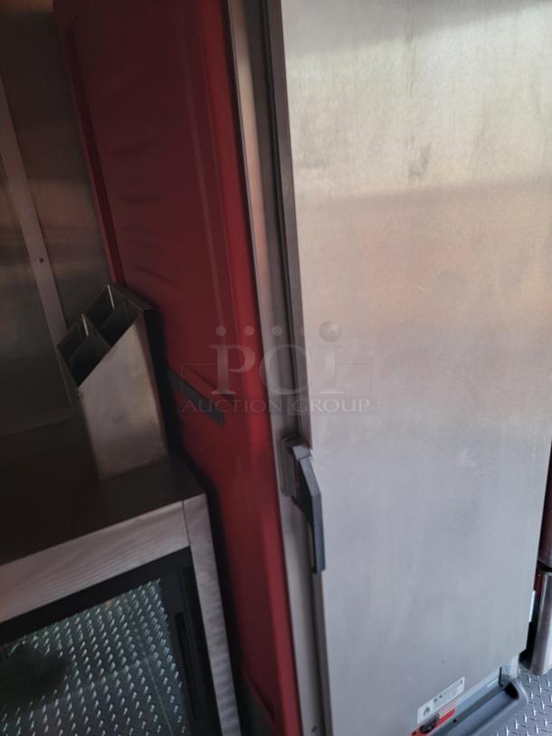 Industrial metal storage cabinet with stainless steel door, red side panel, and black handle on a textured metal floor, used condition.
