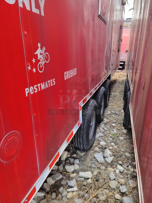 Red food delivery trailer with Postmates and Grubhub branding, triple axle, showing minor wear on rocky terrain.