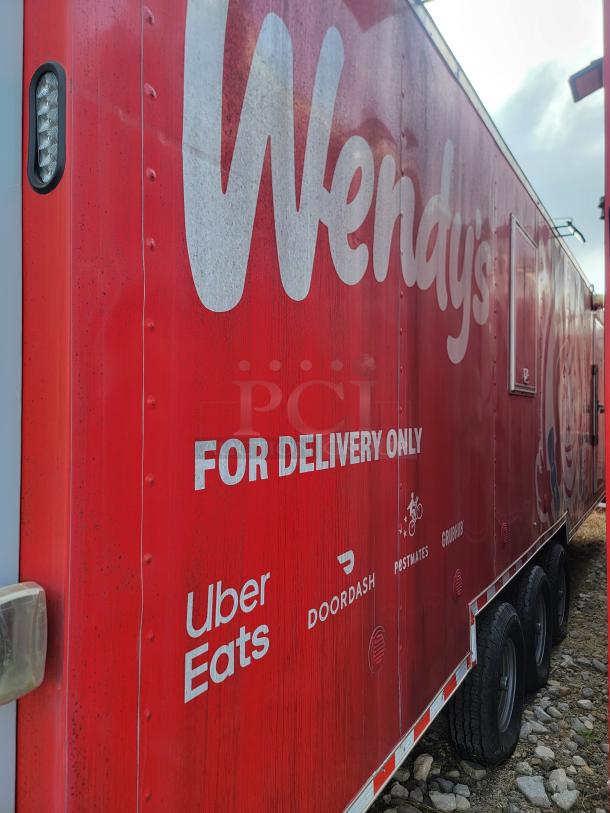 Red mobile food trailer with "Wendy's" logo, "For Delivery Only" text, and delivery service logos. Triple axle wheels.