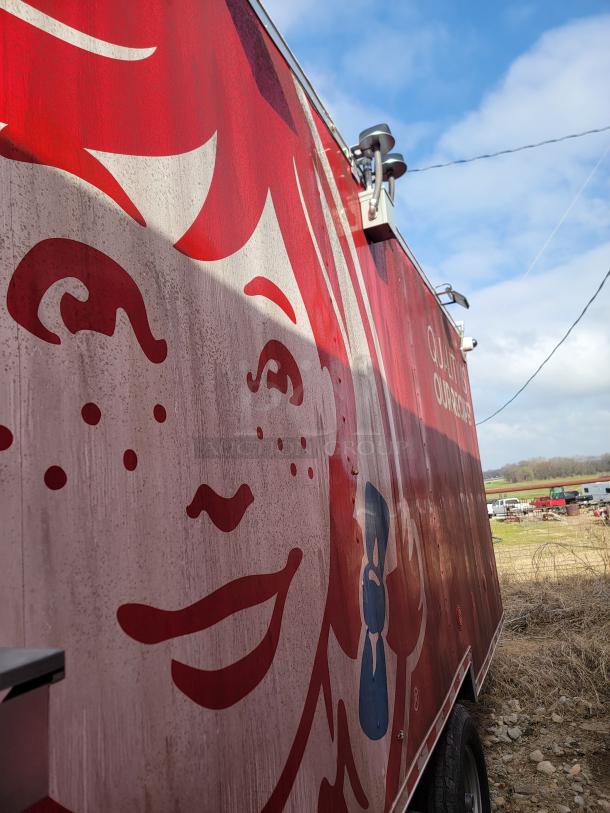Red and white food trailer with a cartoon character face design. Exterior shows signs of wear and dirt.