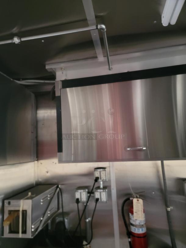 Stainless steel commercial kitchen cabinet in good condition, mounted above electrical outlets and a fire extinguisher.