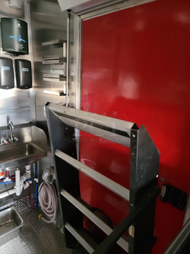 Stainless steel kitchen interior with metal racks, red sliding door, paper towel dispensers, and sink. Industrial setting.