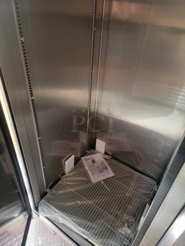 Stainless steel interior cabinet with shelf, protective wrapping, assembly instructions, and mounting hardware visible inside.