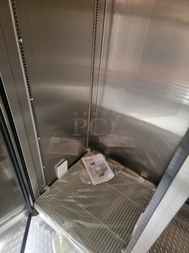 Stainless steel commercial refrigerator interior with shelving and Turbo Air manual, indicating new condition.